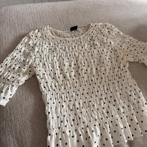 Vit prickig topp från Gina Tricot - Säljer en vit topp med svarta prickar från Gina Tricot. Toppen har trekvartsärm och en smockad design som ger en fin passform. 