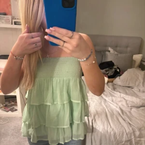 Grön kjol/topp - Säljer en söt grön kjol/axelbandslös topp från Vero Moda. Kjolen har flera lager med volanger och passar lika bra dom topp.