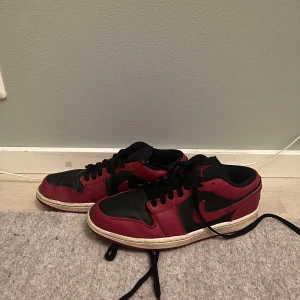 Nike Air Jordans i svart och rött - Snygga Nike Air Jordans i svart och rött med klassisk design. Skorna har en svart bas med röda detaljer och vit sula. Perfekta för dig som vill ha en stilren och sportig look. Skorna har snörning för bästa passform.