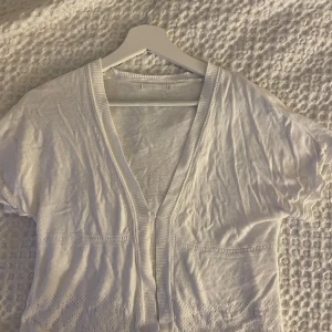 Vit kortärmad kofta - Säljer en söt vit kofta med korta ärmar och fina spetsdetaljer. Koftan har en v-ringad design och knappar framtill. Perfekt för en somrig look! skriv för fler bilder eller frågor!💕🌺