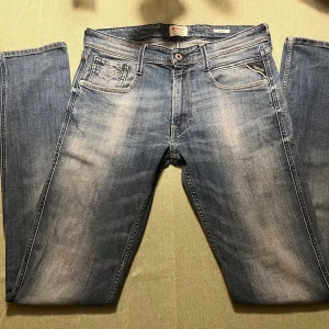 Blå jeans från Replay - Snygga blå jeans från Replay, modell Anbass. De har en klassisk femficksdesign med dragkedja och knapp. Jeansen har en lätt tvättad look och är perfekta för en avslappnad stil.