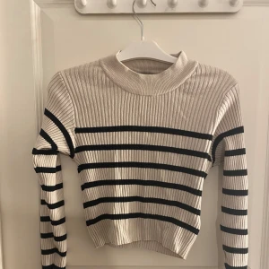 Beige och svart randig ribbad tröja - Säljer en snygg beige tröja med svarta ränder. Tröjan är ribbad och har en croppad passform med långa ärmar. Perfekt för en stilren look.