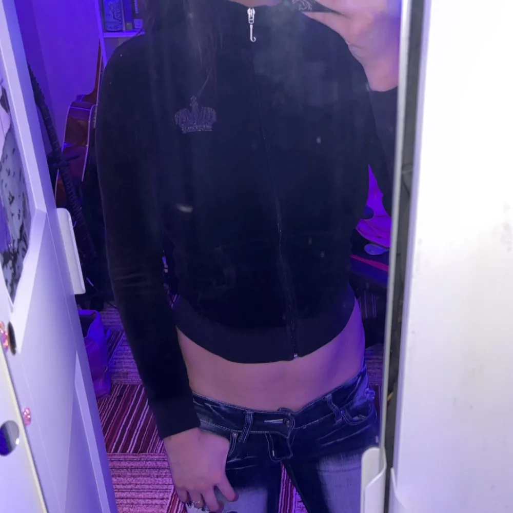 Snygg svart velourjacka från Juicy Couture med dragkedja och glittrande detaljer. Jackan har en tight passform och långa ärmar. Perfekt för en trendig look med en touch av glamour.. Takit.