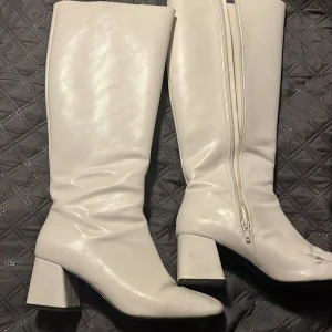 Vita stövlar med klack och dragkedja - Snygga vita stövlar med klack och dragkedja på sidan. De har en spetsig tå och är perfekta för att ge en stilren look. Passar bra till olika outfits och tillfällen.