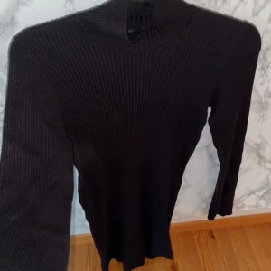 Svart ribbad klänning från Lindex - Snygg svart ribbad klänning från Lindex i storlek S. Klänningen har en polokrage och långa ärmar, perfekt för kyligare dagar. Den är stilren och enkel att matcha med olika accessoarer.