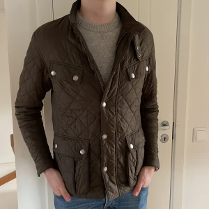 Olivgrön quiltad jacka från Barbour - Säljer en snygg olivgrön quiltad jacka från Barbour. Jackan har en stilren design med knappar och dragkedja framtill samt flera praktiska fickor. Perfekt för höst och vår! Nypriset ligger på runt 3000. Jackan är nästan som ny i skicket.