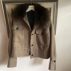 Meotine jacka - Snygg beige/grön jacka från meotine med en lyxig pälsdetalj på kragen. Jackan har knappar framtill och två stora fickor med knappar. Perfekt för att hålla stilen i kyligare väder.