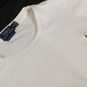 Vit t-shirt från Ralph Lauren - Säljer en klassisk vit t-shirt från Ralph Lauren med broderad logotyp på bröstet. T-shirten har en rund hals och är kortärmad, perfekt för en stilren look. Custom slim fit för en modern passform.