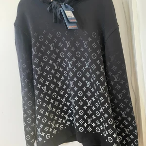 Svart hoodie från Louis Vuitton - Snygg svart hoodie från Louis Vuitton med det ikoniska monogrammönstret i grått. Tröjan har en justerbar huva med snören och långa ärmar. Perfekt för en stilren och lyxig look.
