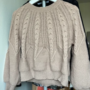 Beige rosa stickad tröja - Mysig beige stickad tröja med kabelstickat mönster. Perfekt för kyliga dagar med sin varma och bekväma design. Tröjan har långa ärmar och en rund halsringning.