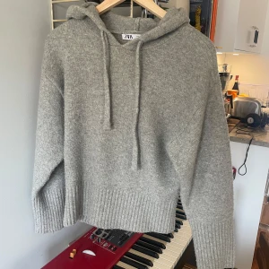 Grå stickad hoodie från Zara - Mysig grå stickad hoodie från Zara med långa ärmar och en bekväm passform. Perfekt för kyliga dagar med sin ribbade nederkant och muddar. Jag har använt den ett få tal gånger men den är i jättefint skick!❤️