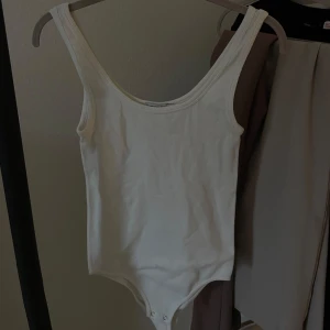 Vit ribbad bodysuit - Säljer en stilren vit ribbad bodysuit med breda axelband. Perfekt för lager-på-lager eller att bära som den är. Enkel och mångsidig design. Använd fåtal gånger och har en skön och bra passform. Kom privat för fler bilder 
