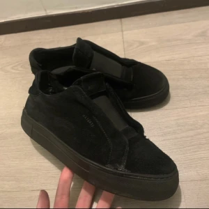 Svarta sneakers från Axel Arigato - Snygga svarta sneakers från Axel Arigato i mocka. Skorna har en stilren design utan snörning och en tjock sula som ger en modern look. Perfekta för en minimalistisk stil.