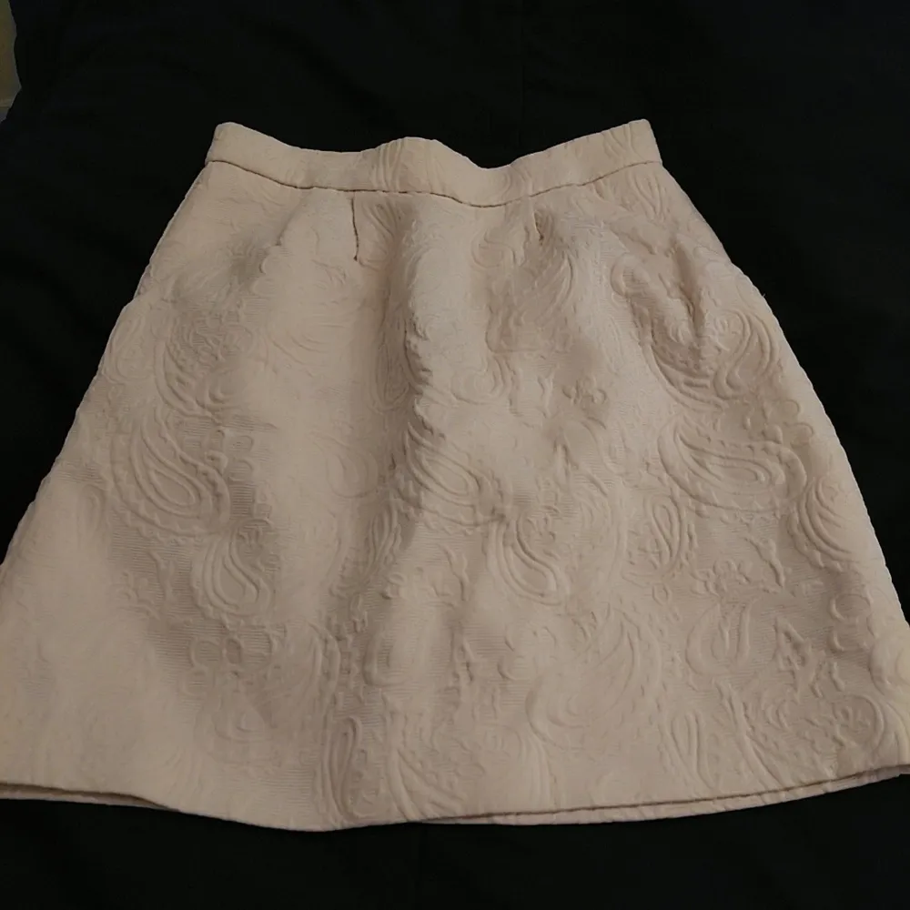 Snygg beige kjol från H&M med ett subtilt mönster i tyget. Kjolen har en klassisk A-linjeform och är perfekt för en stilren look. Den är i storlek 34 och passar perfekt för dig som gillar en elegant stil.. Hameet.