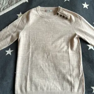 Säljer en stilren beige tröja från J.Lindeberg i 100% merinoull. Tröjan har långa ärmar och knappar vid axeln för en snygg detalj. Perfekt för kyligare dagar! Den är helt oanvänd och passar mer XS än S. Perfekt tröja till våren!!!