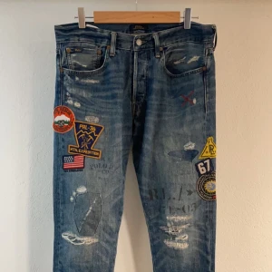 Jeans med patches från Polo Ralph Lauren - Snygga blå jeans från Polo Ralph Lauren med coola patches och slitningar. Unika och har inte hittat många par ute till försäljning. Perfekt statement piece