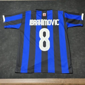 Blå och svart randig fotbollströja - Snygg blå och svart randig fotbollströja med korta ärmar och nummer 8 på ryggen. Perfekt för fotbollsfans som vill visa sitt stöd. Namnet 'Ibrahimovic' pryder ryggen.