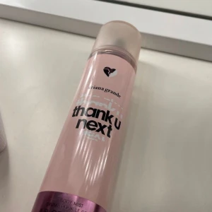 Thank U Next Body Mist av Ariana Grande - Säljer en rosa body mist från Ariana Grande med namnet 'Thank U Next'. Flaskan har en stilren design med ett hjärta på toppen och text i svart. Perfekt för en lätt och fräsch doftupplevelse.