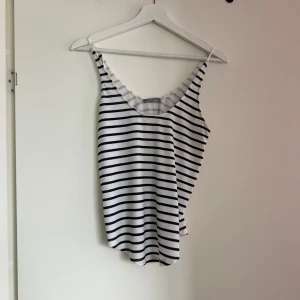 Randig linnetopp från Zara - Säljer en stilren randig linnetopp från Zara. Toppen är vit med svarta ränder och har en klassisk design med smala axelband. Perfekt för varma dagar eller som ett lager under en jacka.