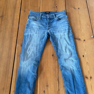 Blå jeans från Jack & Jones - Snygga blå jeans från Jack & Jones med klassisk femficksdesign och en bekväm passform. De har en lätt tvättad look och en läderpatch med logotyp baktill. Perfekta för en avslappnad eller stilren look.