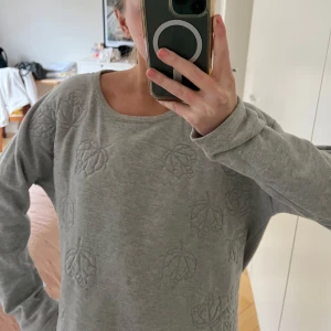 Grå sweatshirt  - Säljer en mysig grå tröja med subtilt bladmönster. Tröjan har långa ärmar och en rund halsringning. Mycket bra skick!!