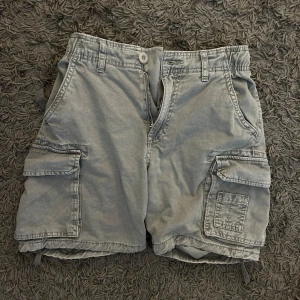 Grå cargo shorts från Bershka - Säljer ett par grå cargo shorts från Bershka. De har flera praktiska fickor och en dragkedja framtill. Perfekta för en avslappnad stil. Passar bra till sommarens äventyr.