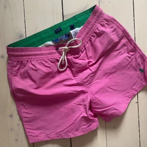 Rosa badshorts från Polo Ralph Lauren - Rosa badshorts/badbyxor från Polo Ralph Lauren med grön insida och snörning i midjan.
