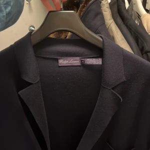Ralph Lauren purple label blazer  - Snygg mörkblå kofta från Ralph Lauren med dubbelknäppning och stilrena knappar. Kavajen har flera fickor och en klassisk krage. Perfekt för en elegant look. Kashmir och bomull 
