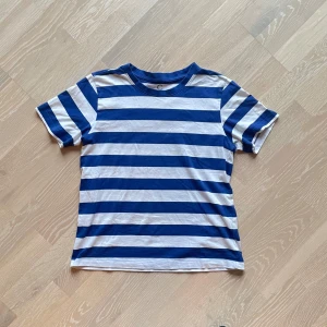Blå och vit randig t-shirt från Cubus - Säljer en blå och vit randig t-shirt med korta ärmar. Perfekt för en avslappnad stil. T-shirten har en klassisk rund halsringning och är tillverkad i ett mjukt material. Perfekt till sommarens långa dagar! 🌝