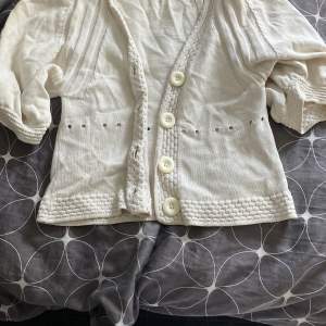 Säljer en söt vit kofta från H&M med stora knappar framtill. Koftan har trekvartsärmar och ett fint ribbat mönster vid ärmslut och nederkant. Perfekt för en stilren look!