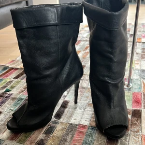 Ance klackar - Snygga svarta stövletter i skinn med hög klack och öppen tå från acne. De har en stilren design med en uppvikt kant upptill som ger en unik look. Perfekta för att lyfta vilken outfit som helst. Man kan ha dem vikta där uppe och vika mer ner om man vill ha dem kortare  eller bara vika ur dem och ha dem så.
