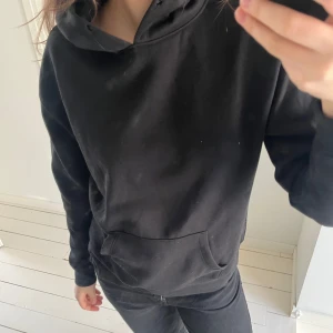 Svart hoodie - Säljer en klassisk svart hoodie med känguruficka framtill. Perfekt för en avslappnad stil och enkel att matcha med andra plagg. Den har långa ärmar och en bekväm passform.