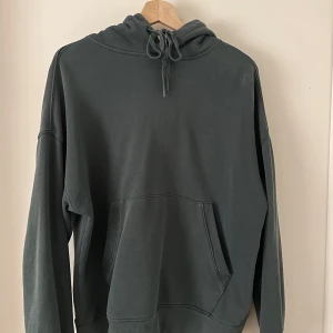 Mörkgrön hoodie från Junkyard - Säljer en stilren mörkgrön hoodie från Junkyard. 70% bomull och 30% polyester. Stor i storleken, sitter lite baggy på mig som bär kvinna 36/38 s/m i vanliga fall. Den har en klassisk design med en stor ficka framtill och justerbar huva med dragsko. 