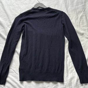 Marinblå tröja från J.Lindeberg - Snygg merinoull  tröja från J.Lindeberg i storlek S. Tröjan har en liten defekt under ärmen men inget som syns vid användning. Nypris: 1300kr