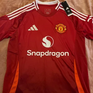 Röd Manchester United matchtröja - Snygg röd Manchester United matchtröja från årets säsong med vita detaljer och klubbens emblem på bröstet. Är storlek M men rätt stor, kan tolkas som L. 