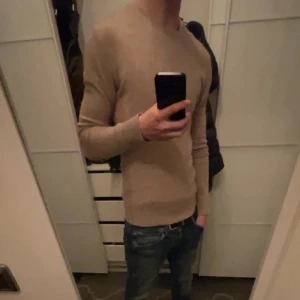 Beige kashmirtröja från J.Lindeberg  - Säljer en stilren beige kashmirtröja från J.Lindeberg. Tröjan har en rund halsringning och ribbstickade muddar vid ärmslut och nederkant. Finns något väldigt litet hål som inte märks av vid användning.Perfekt för en elegant och bekväm look. Storlek S och vid frågor är det bara att ställa de!