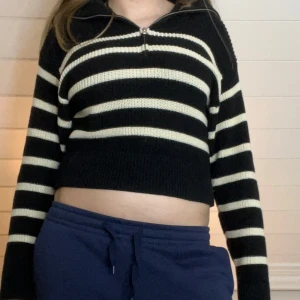 Svart och vit randig stickad tröja - Säljer en svart och vit randig stickad tröja med dragkedja framtill. Tröjan är lite liten på mig därför ser den croppad ut, och har långa ärmar, perfekt för en avslappnad stil. Den är både bekväm och trendig.