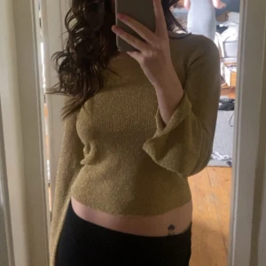 Guldglittrig tröja - Snygg guldglittrig tröja med långa ärmar och en croppad passform. Perfekt för att lysa upp vilken outfit som helst. Tröjan har en elegant och festlig känsla, vilket gör den idealisk för speciella tillfällen.