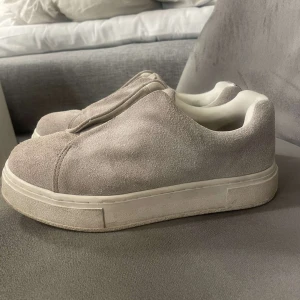 Grå sneakers från Eytys - Snygga grå sneakers från Eytys i mocka med en stilren design utan snörning. Skorna har en tjock vit sula och en bekväm passform. Används 4 gånger så nästintill nya. Storlek 37 men passar även 38