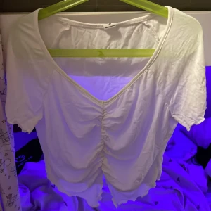 Vit topp  - Säljer en vit topp från SHEIN Med veringning samt ett resårband framtill vilket man kan se på första bilden, toppen är även lite öppen nertill vilket man kan se på andra bilden ⭐️ den har gjorts i ett tunt material och är tyvärr ganska genomskinlig. 