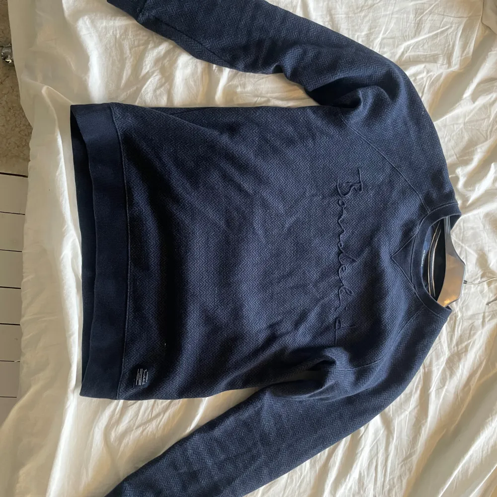 Säljer en snygg mörkblå tröja från Bondelid med broderad logga på bröstet. Tröjan har en klassisk passform och är perfekt för en stilren look. Den är långärmad och gjord i ett mjukt material.. Neuletakit & Villapaidat.