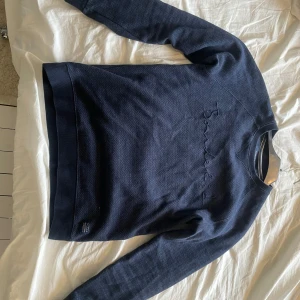 Mörkblå tröja från Bondelid - Säljer en snygg mörkblå tröja från Bondelid med broderad logga på bröstet. Tröjan har en klassisk passform och är perfekt för en stilren look. Den är långärmad och gjord i ett mjukt material.