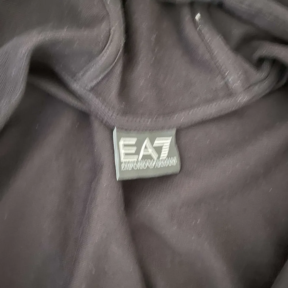 Säljer en stilren svart hoodie från EA7 med dragkedja och luva. Perfekt för en avslappnad look. Den har en liten logga på bröstet och är tillverkad i ett mjukt material. Den helt ny inte använd priset kan diskuteras . Neuletakit & Villapaidat.