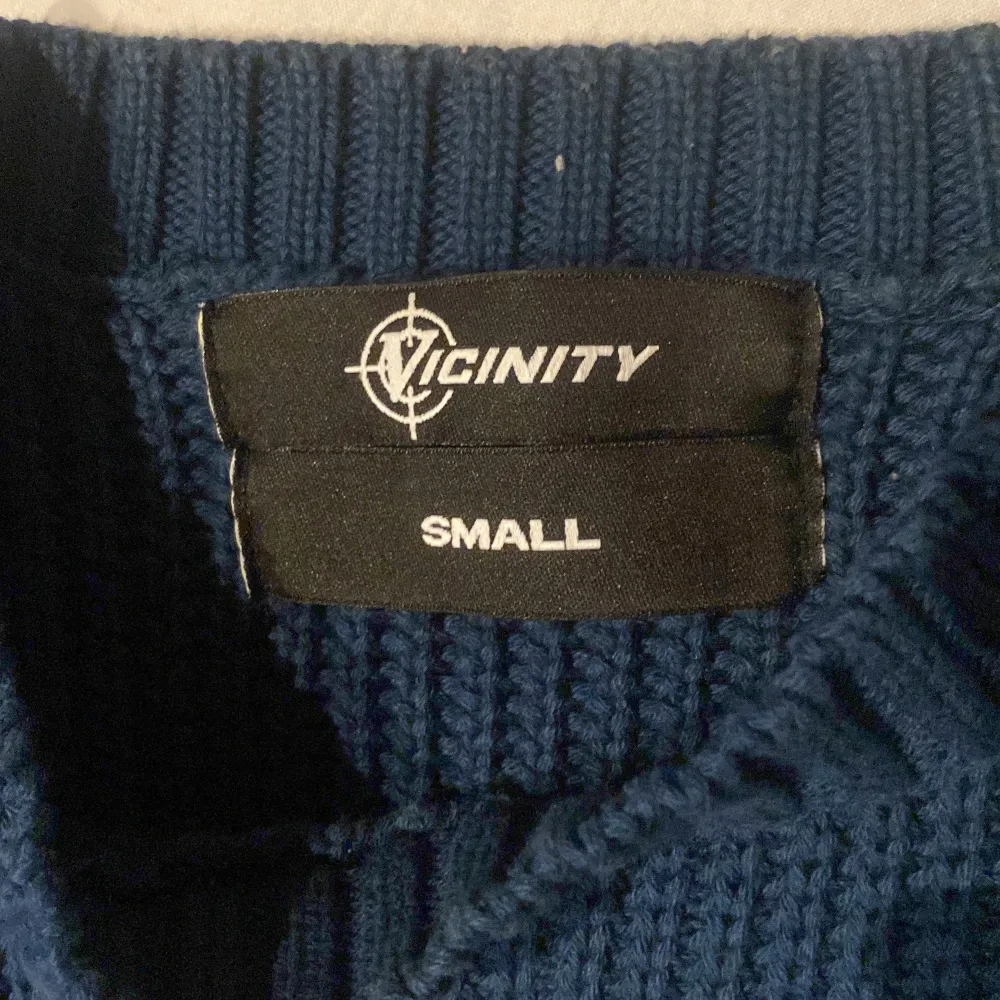 Säljer en snygg blå stickad tröja från Vicinity med ett stort vitt emblem på framsidan. Tröjan har långa ärmar och ribbade kanter som ger en skön passform 10/10 kvalite . Neuletakit & Villapaidat.