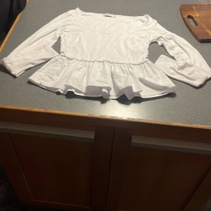 Vit långärmad topp från Stradivarius - Säljer en söt vit topp från Stradivarius med volangdetalj i nederkant. Toppen har långa ärmar och en rund halsringning. Perfekt för en stilren look. Köparen står för frakt!❣️