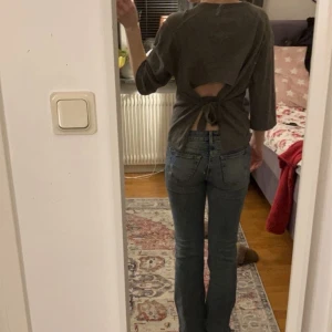 Grå tröja med knytning bak - Säljer en stilren grå tröja med v-ringning och trekvartsärmar. Tröjan har en unik design med öppen rygg och knytning bak, vilket ger en trendig look. Perfekt för att lägga till en twist i din garderob!