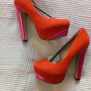 Orange och rosa pumps med hög klack. - Snygga pumps i orange mocka med rosa lackdetaljer och hög klack. Perfekta för att ge en färgklick till din outfit. Klacken mäter 14 cm och skon är stabil med bekväm passform. Helt nya 