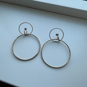 Guldiga hoop-örhängen - Stilrena guldiga hoop-örhängen med dubbla cirklar. Perfekta för att ge en elegant touch till din outfit. De är lätta och bekväma att bära hela dagen.