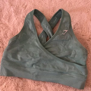Blå sporttopp från Gymshark - Snygg turkosblå sporttopp från Gymshark med korsade axelband och ribbad kant. Perfekt för träning med sin bekväma passform och stilrena design.