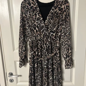 Leopardmönstrad klänning - Trendig leopardmönstrad klänning med omlott-design och långa ärmar. Perfekt för att sticka ut med stil. Jag vet inte riktigt vilken storlek det är då det inte står men skulle säga runt storlek S